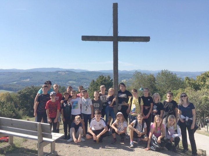 eine Schulklasse steht bei blauem Himmel vor dem Gipfelkreuz