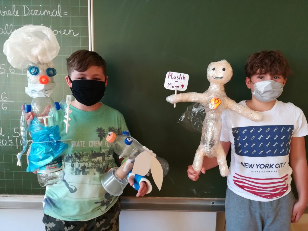 Zwei Burschen zeigen ein Männchen aus Plastik und ein Männschen aus Plastikflaschen in die Kamera.