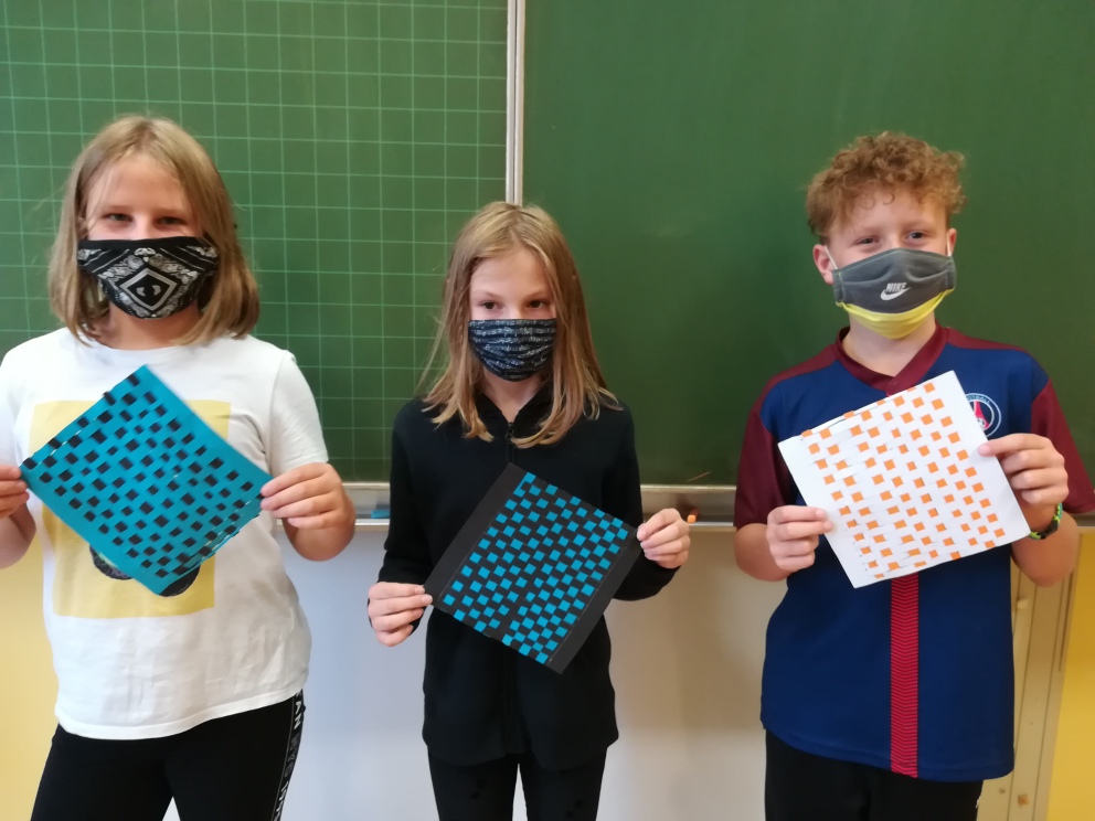 drei Jugendliche haben Masken auf und halten ihre Werkprojekte in die Kamera.